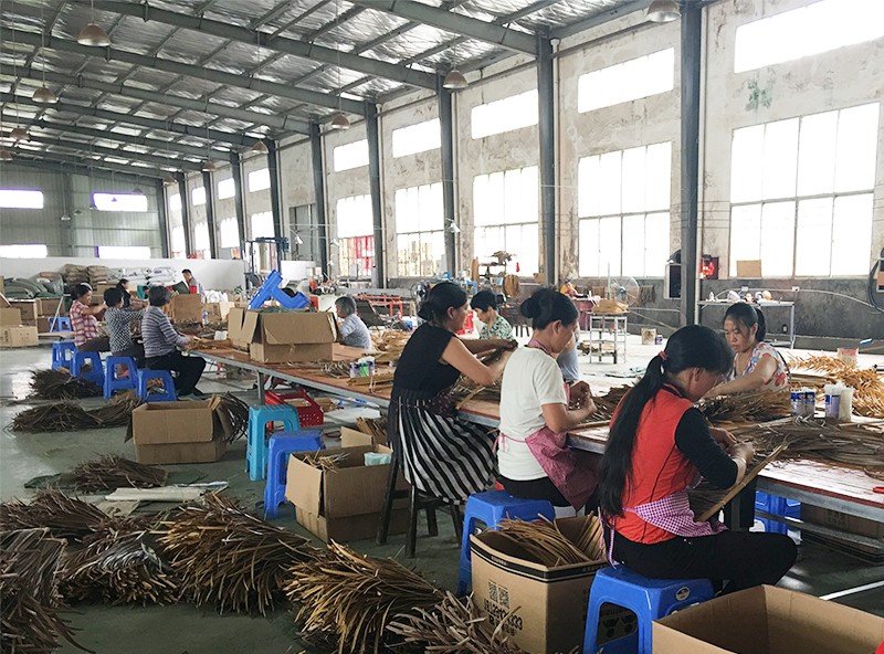 Hand-assembly workshop — workers bundling palm-profile thatch panels for export orders